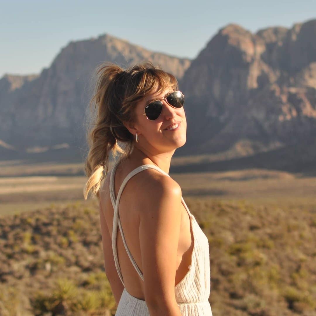 A woman in a white dress standing in front of a mountain.