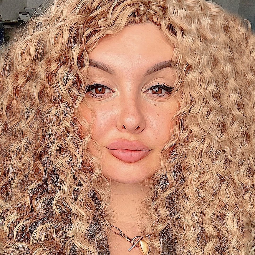 A woman with long curly hair is posing for a photo.