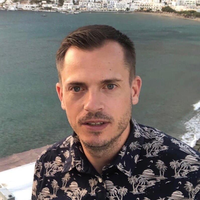 A man in a hawaiian shirt standing in front of the ocean.