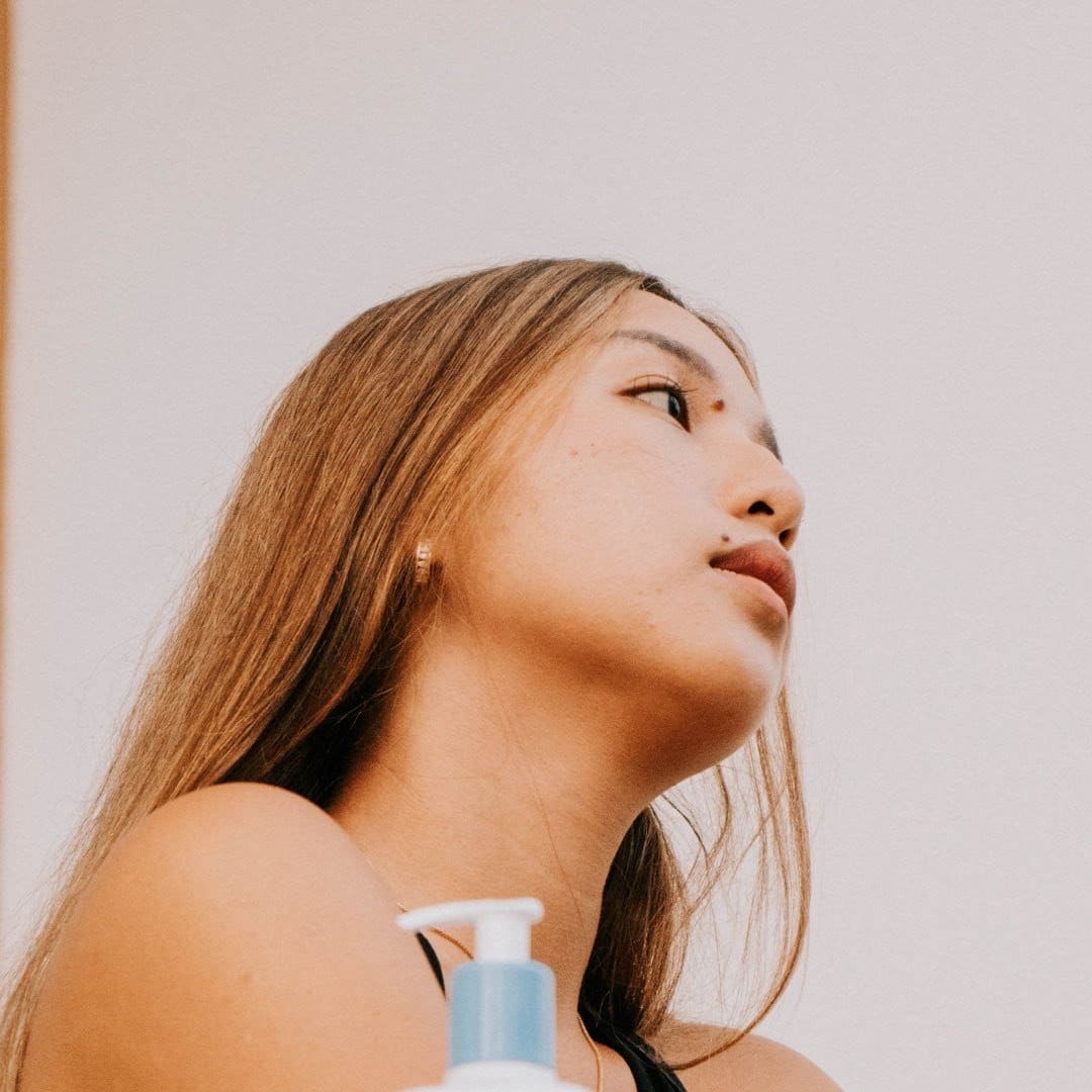 A woman looking up at a bottle of lotion.