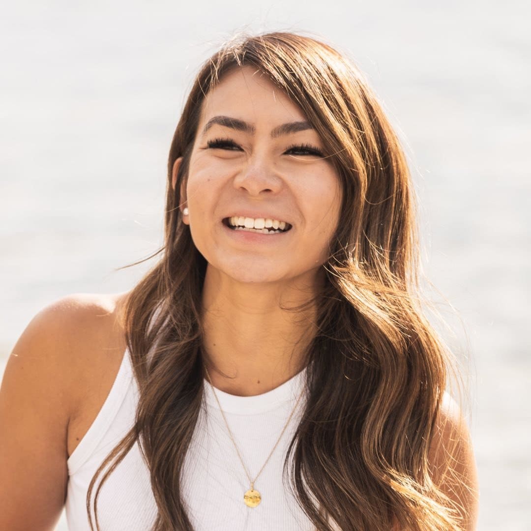 A smiling woman wearing a white tank top and a necklace.